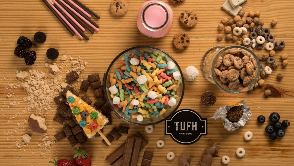 Interior de Tufh Cocina Urbana con una mesa mostrando un waffle con frutas y un batido de cereal, luz cálida y clientes disfrutando