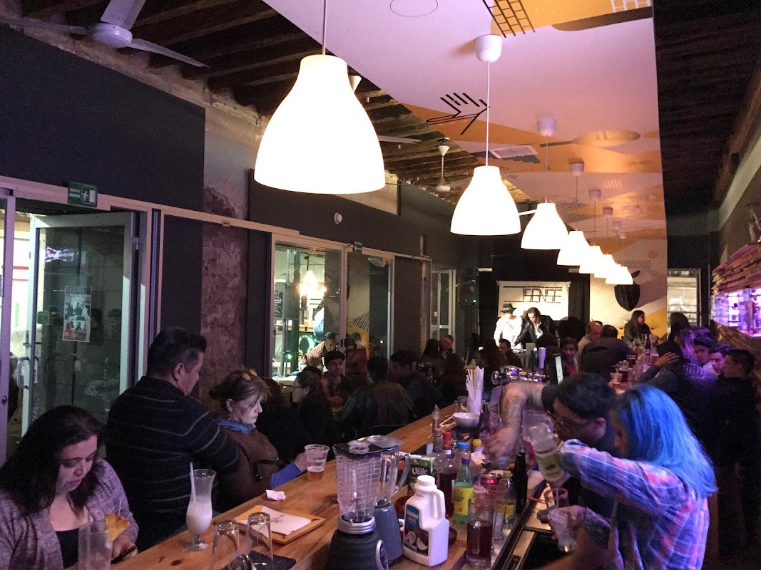 Interior con barra, botellas de cerveza y clientes charlando, luz cálida y música en vivo