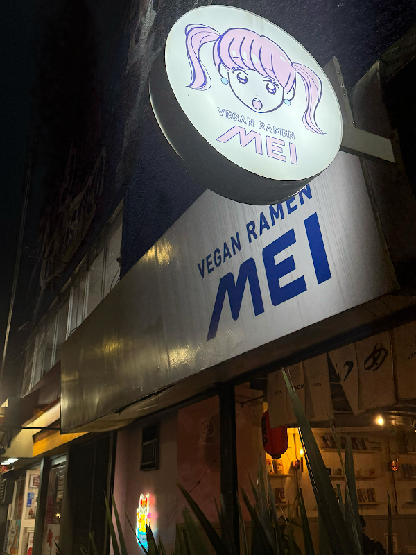Exterior de Vegan Ramen Mei Del Valle en Félix Cuevas, luces de neón y fachada de vidrio, con clientes entrando al anochecer