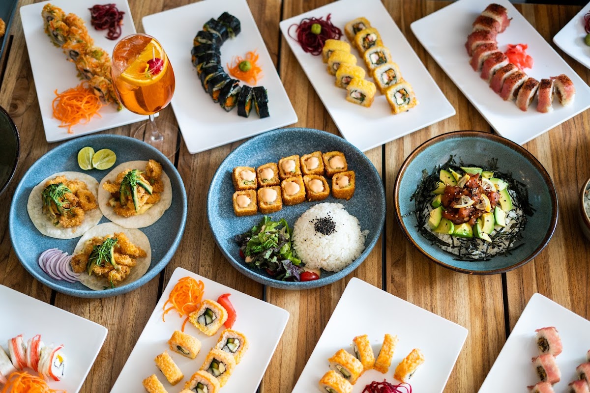 Hand rolls arranged on a black plate with soy sauce and garnishes