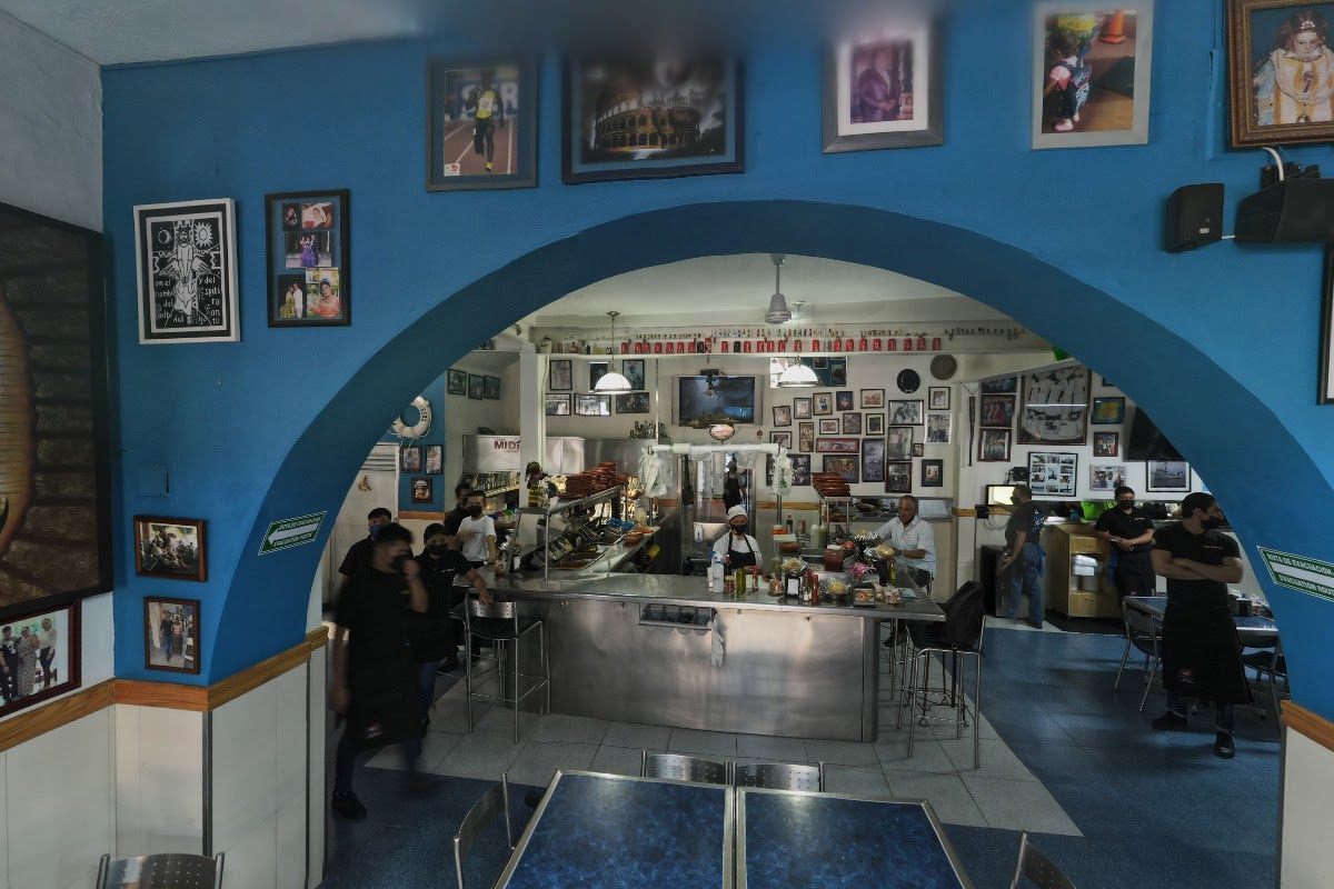Taco Fish La Paz storefront on Av. de la Paz with colorful signage and a bustling outdoor patio, showing a plate of shrimp tacos.