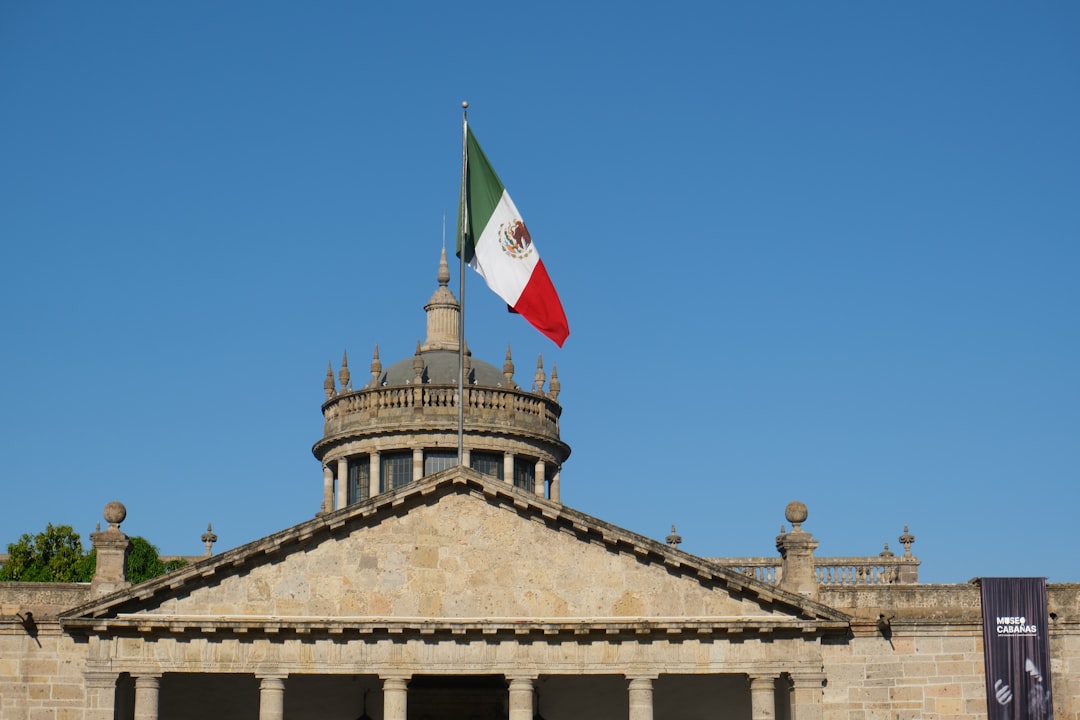 The mexican flag flies above a stone building.