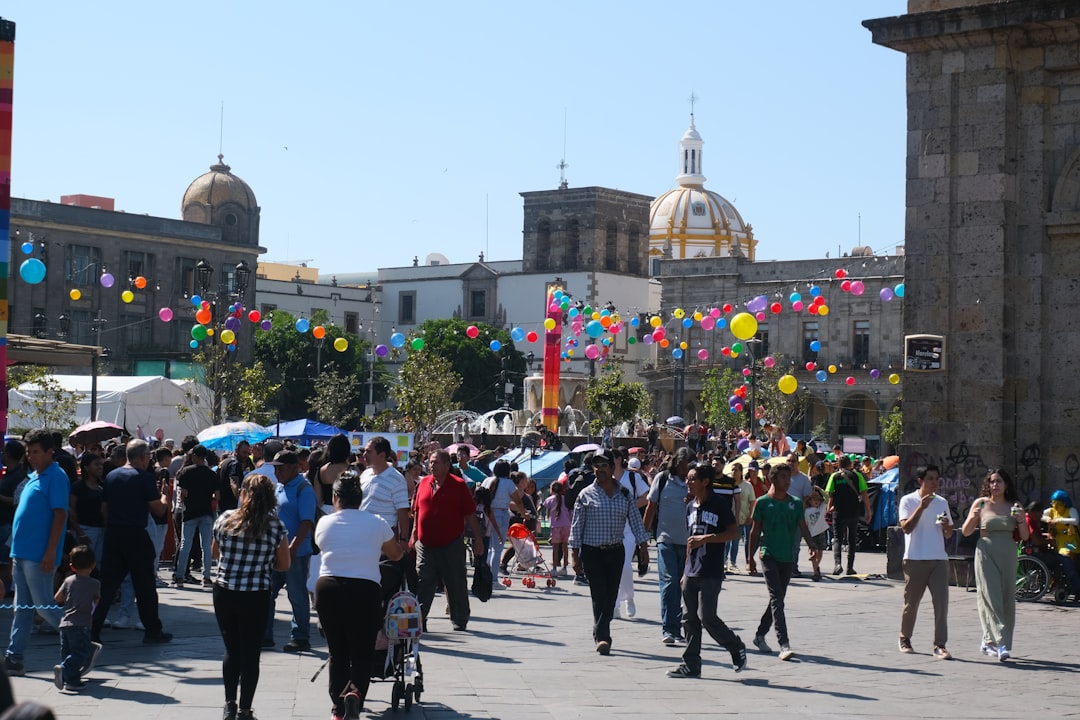 People gather in a sunny plaza with colorful balloons.