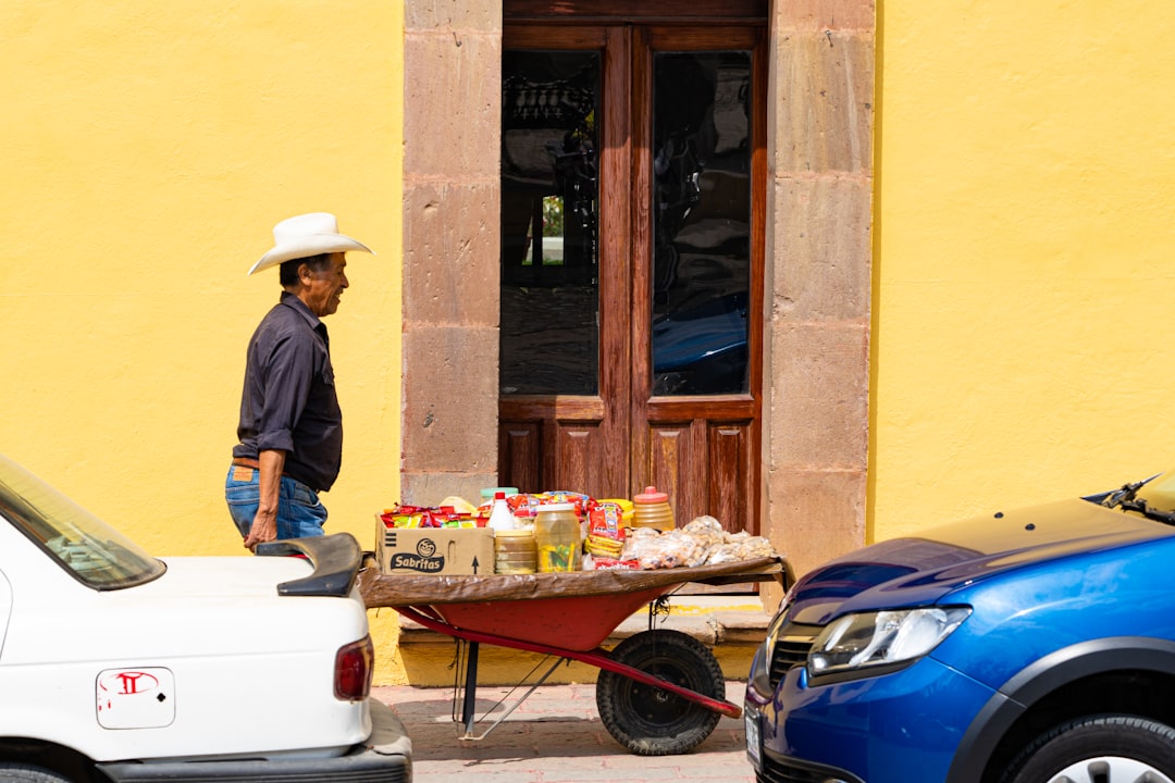 man in blue dress shirt and brown hat standing beside brown wooden door during daytime