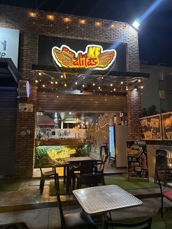 Exterior of KFAlitas Jardines del Río at night, neon sign glowing, street view with patrons entering