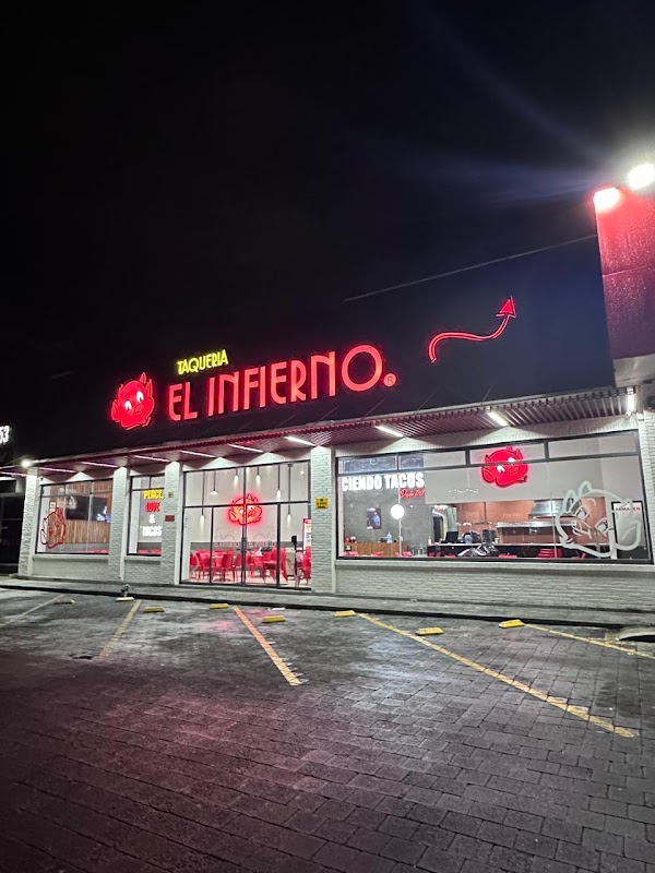 Exterior night view of Taquería El Infierno Camelinas with neon sign glowing, street and pedestrians visible