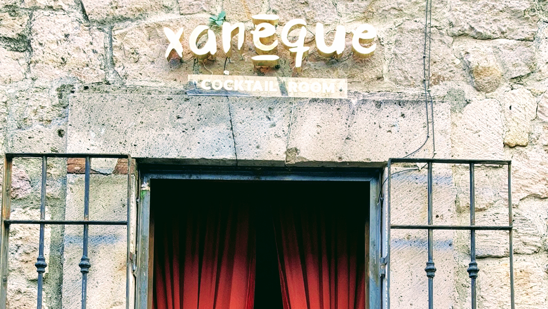 Exterior of Xaneque Cocktail Room on Del Romance, showing its modest façade and illuminated sign at night