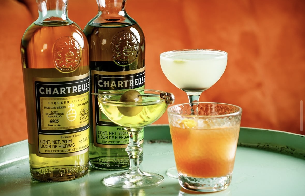 Interior de Xaneque Cocktail Room con barra iluminada, copas de cóctel y vinilos en la pared