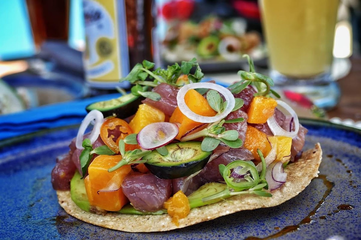 Tacos de pescado en CardOmen Oaxaca, mostrados en una tabla de madera, con salsa de aguachile y mezcal al fondo