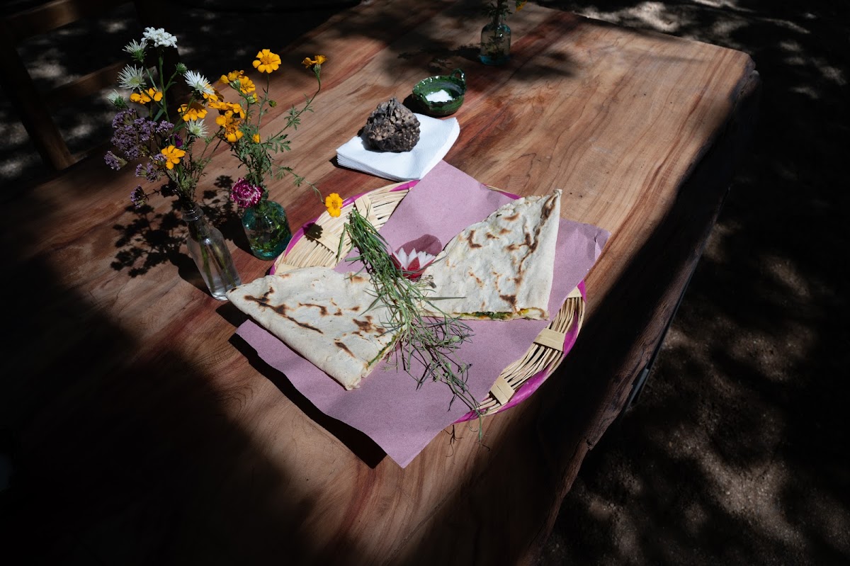 Adamá – cozy dining area with a chalkboard menu, a plate of tlayuda and a glass of mezcal