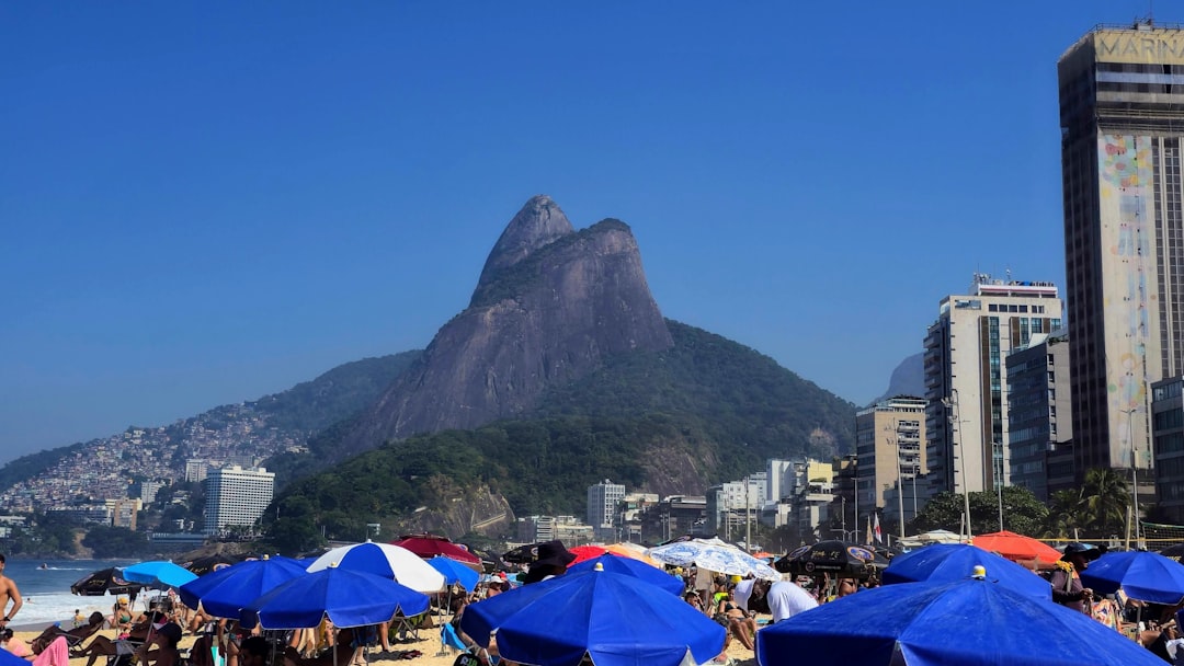 a crowded beach with blue umbrellas and a mountain in the background