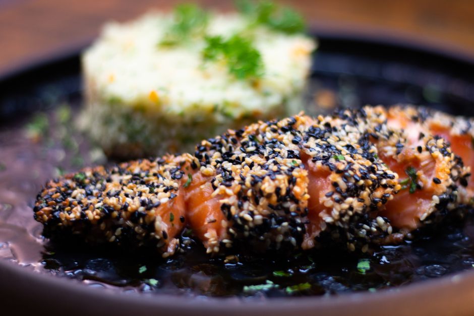 Close-up of sesame crusted salmon with rice on a stylish black plate, showcasing gourmet food photography.