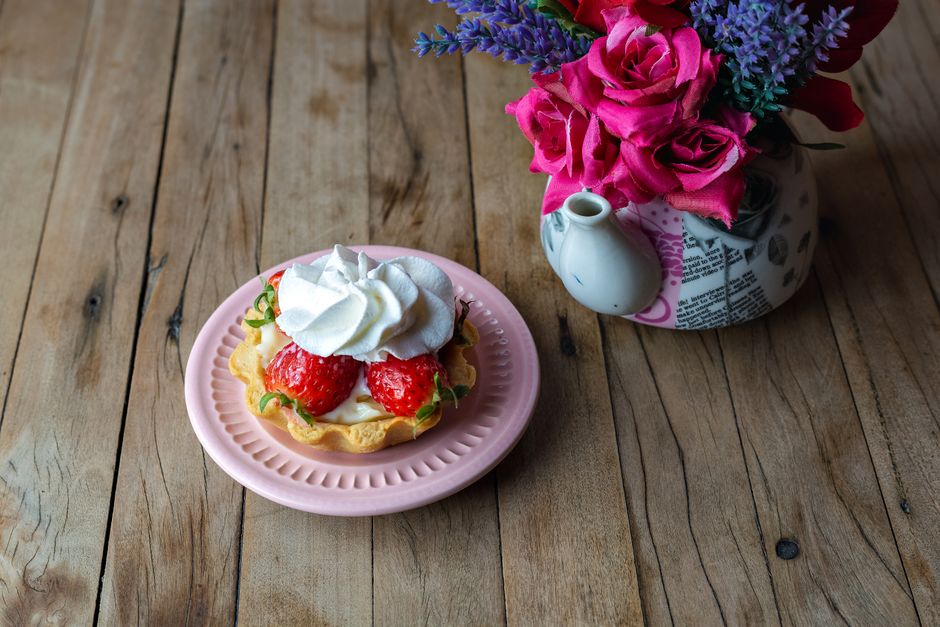 A delicious strawberry tart with whipped cream next to a vibrant floral arrangement on a wooden table.