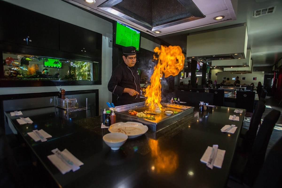 Sushi Factory – vista del mostrador de sushi con chefs preparando nigiri, enfoque en pescado brillante y limón