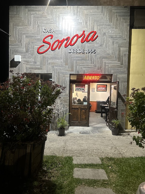 Exterior colorida de Casa Sonora con su letrero y una tabla de tacos de carne asada al estilo Sonora