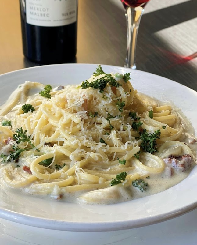 Exterior de Quattro Fogon Italiano con su letrero rojo y una mesa al aire libre, mostrando el tagliatelle al ragú en primer plano
